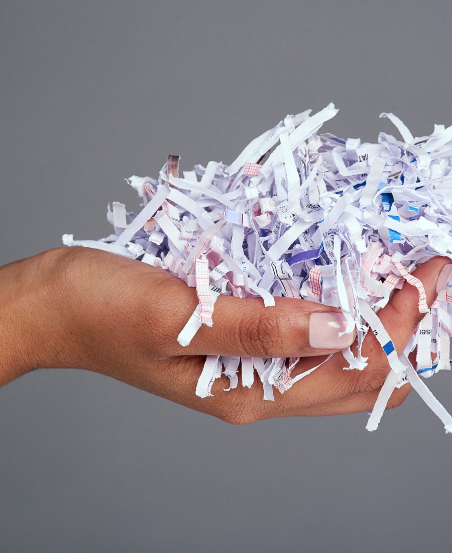 Protect your information. Studio shot of a womans hand holding a Studio shot of a womans hand holding a pile of shredded paper against a grey background.